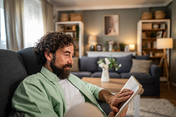 istock Man reading book on couch enjoying cozy leisure time at home 2236937753