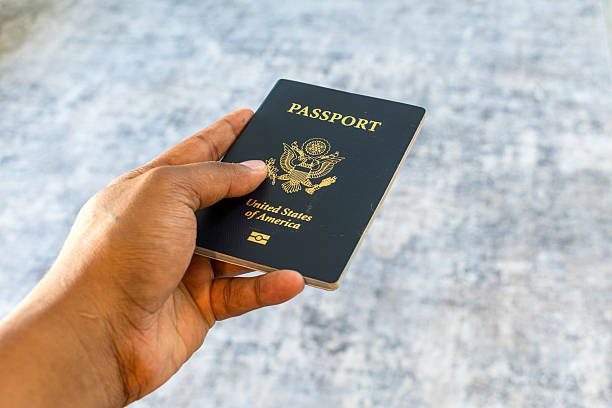 Salt Lake City, Utah, July 15, 2025: A person holds a U.S. passport at an angle near a pale backdrop. Federally issued, it confirms identity and citizenship for international travel.