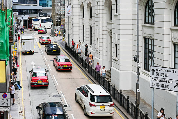 People crossing the road near the Hong Kong Central Market and red taxis waiting at traffic lights