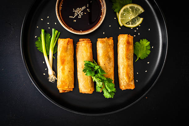 Spring rolls filled with meat and vegetables served with soy sauce on wooden table