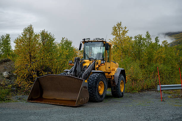 Yellow front loader tractor parked outdoors on gravel with autumn trees