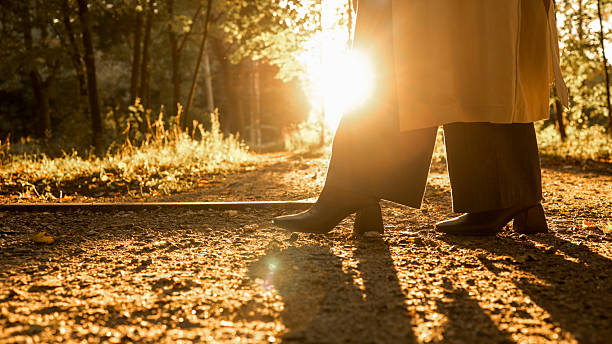 A person is seen walking on a path with the sun shining brightly through the trees, creating a warm and inviting atmosphere.