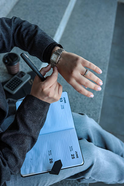 istock Woman checking the time on her watch while sitting with a planner. 2236954735