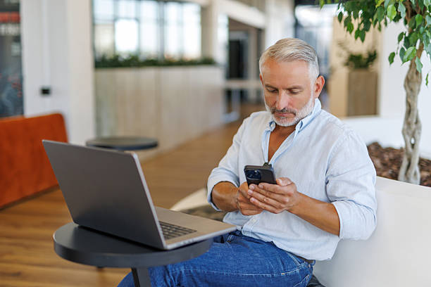 istock Middle aged business manager ceo using cell phone mobile app, laptop. 2236956264