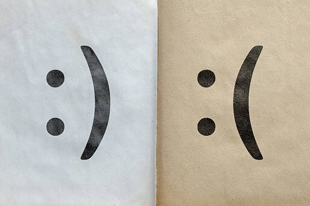 A conceptual and emotionally evocative photograph featuring an open, aged notebook or two distinct paper surfaces. The left page (or surface) is lighter, with a clear happy emoticon face (\