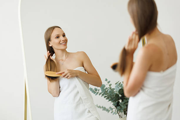 istock Pretty woman brushing her beautiful hair with comb while looking at her reflection and smiling in mirror in bathroom interior 2236959824