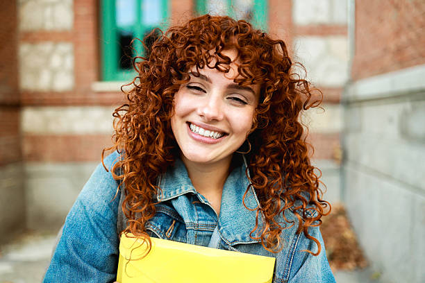 istock Smiling redhead curly student woman with yellow folder on university campus - Back to school concept 2236966159