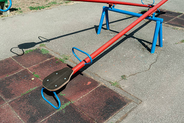 Empty retro seesaw standing still under the daylight. This photo reflects the concept of childhood, balance, absence, solitude, memory, silence, and the fleeting passage of time.