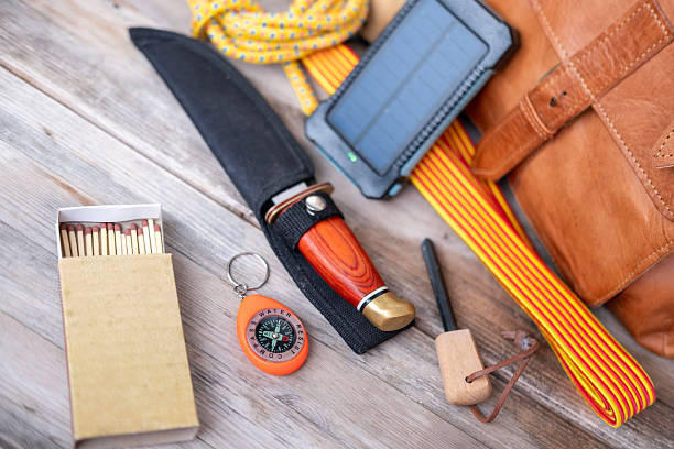 istock Camping gear with leather backpack, solar charger, knife, compass, rope, thermos, survival essentials, Survival equipment on wooden table, survival wilderness kit, outdoor adventure kit 2236977243