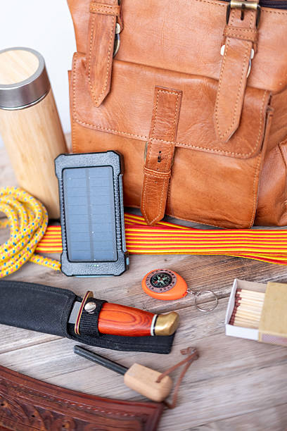 istock Camping gear with leather backpack, solar charger, knife, compass, rope, thermos, survival essentials, Survival equipment on wooden table, survival wilderness kit, outdoor adventure kit 2236977244