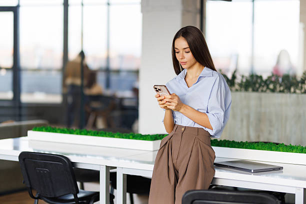istock Young happy business woman looking at smartphone using cellphone mobile cellular tech working in office 2236980343
