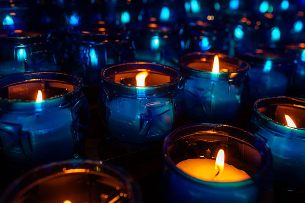 Rows of blue glass candles with glowing flames create a peaceful ambiance, casting warm light and reflections in the surrounding dark space, enhancing the serene environment.