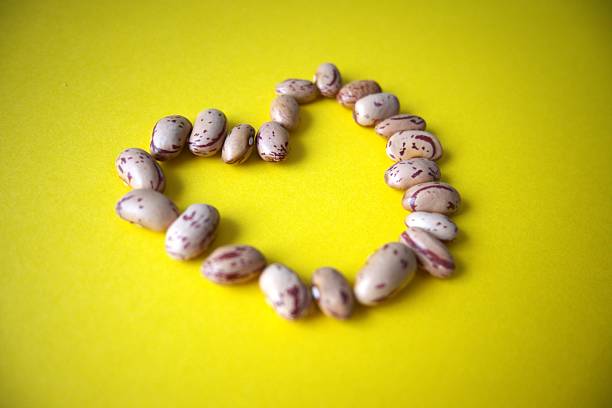 Close-up of heart shape arranged from beans on yellow background with copy space.