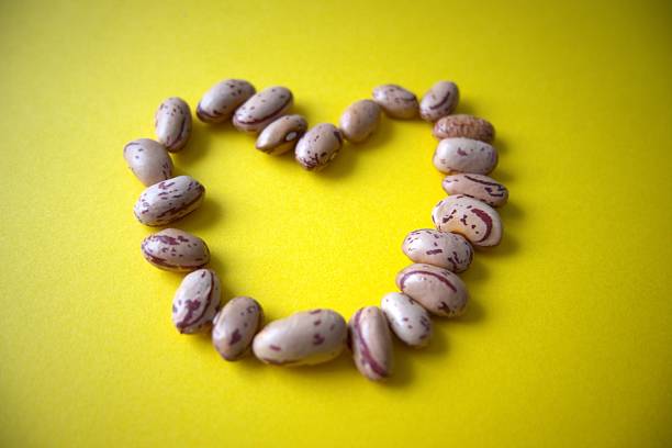 Close-up of heart shape arranged from beans on yellow background with copy space.