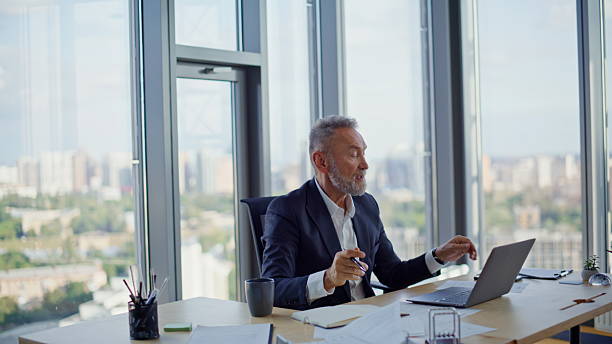 istock Confident manager consulting online talking to laptop webcam showing papers. 2236990114