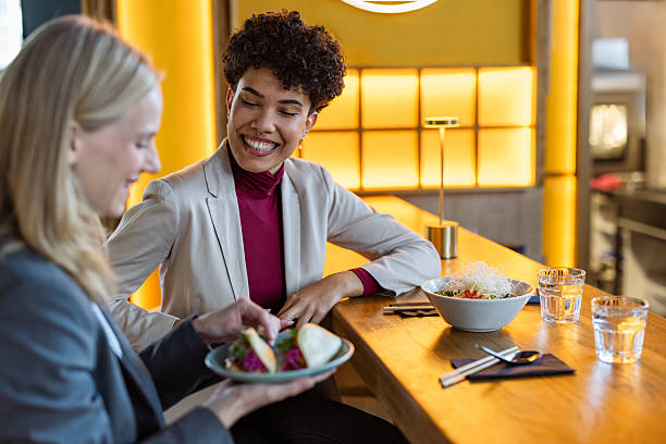 Two businesswomen share a meal during a work break at a restaurant. They chat, connect, and enjoy casual, professional conversation in a modern dining setting.