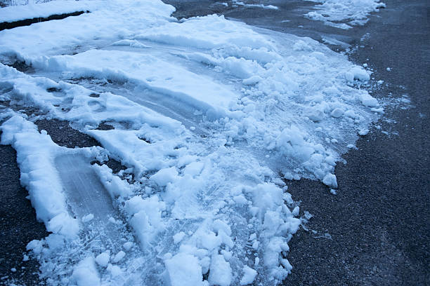 quiet, snow-covered road winds winter landscape, pavement after heavy snowfall, Slippery surface warning, wet snow melts, Cold morning drive, icy snow patches on paved road, hazardous driving surfaces