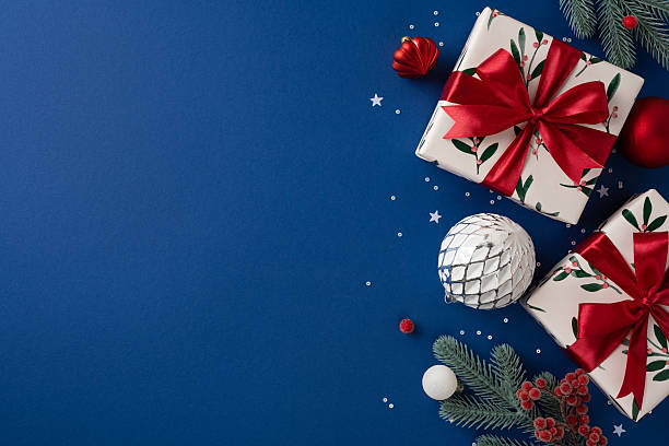 istock Vibrant Christmas display features wrapped presents with red ribbons, silver ornament, pine branches, and decorative stars on a deep blue surface 2236996127