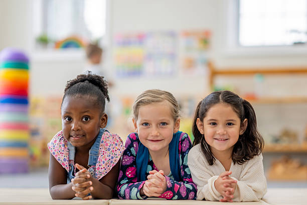 istock Three Diverse Girls Lying at a Table, Smiling Friends in a Bright School Classroom 2236996649