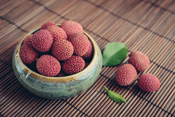 Fresh organic lychee fruit in bowl on bamboo background closeup