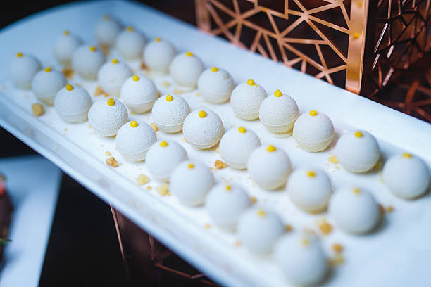 close-up shot of a white rectangular platter displaying numerous identical gourmet white truffles. Each bite-sized sphere is topped with a tiny yellow dot and arranged in neat rows