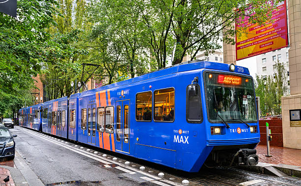 Portland, Oregon - June 21, 2025: A TriMet MAX light rail train travels along a tree-lined street in the downtown core of the city on a wet, overcast day