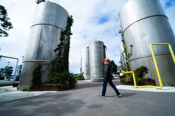 A worker wearing a safety helmet walks through an industrial facility surrounded by large metal storage tanks, highlighting themes of industry, safety, and infrastructure.