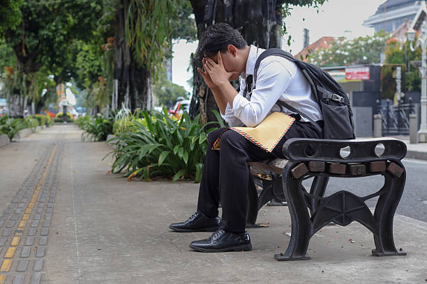 istock Portrait of Asian employee in suit looking for work while holding a brown envelope containing his resume, sitting on bench with hands on head. Job seeker recruitment concept 2237039360
