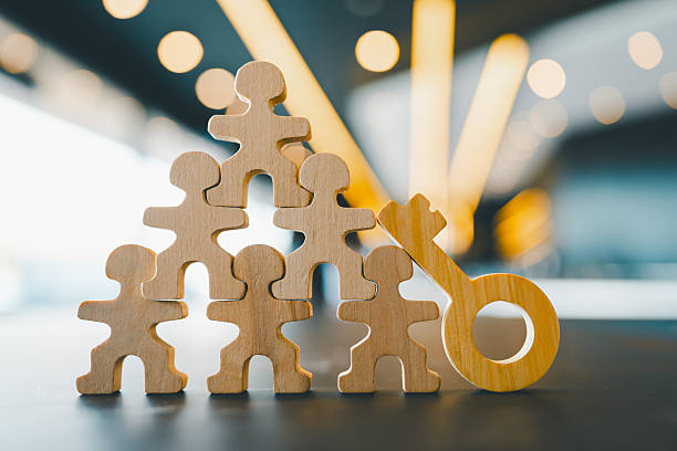 istock Wooden human figures forming a pyramid with a key symbol, representing teamwork, leadership, success, and human resources. Ideal for business concepts, strategy, or collaboration themes. 2237041299