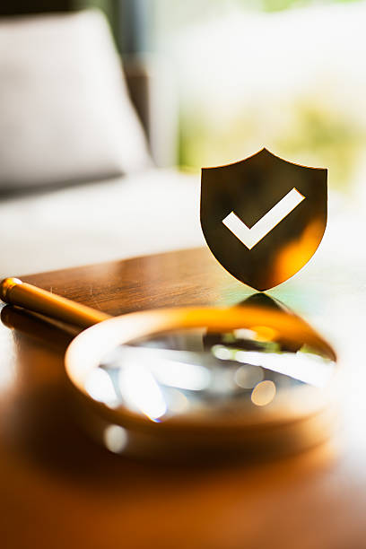 Magnifying glass with shield checkmark symbol on table, representing security inspection, trust verification, quality assurance, cybersecurity, and compliance. Perfect for tech or business content.
