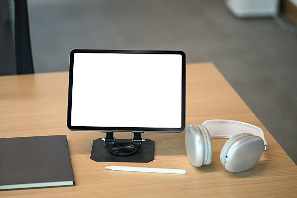 Digital tablet with blank screen on desk beside wireless headphones in modern office.