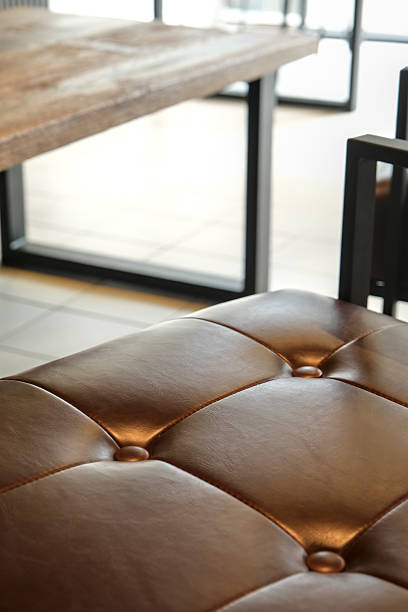 istock Close-up of a brown leather cushion with button tufting, showing texture, stitching, and elegant upholstery detail in warm light. Front view. 2237052196