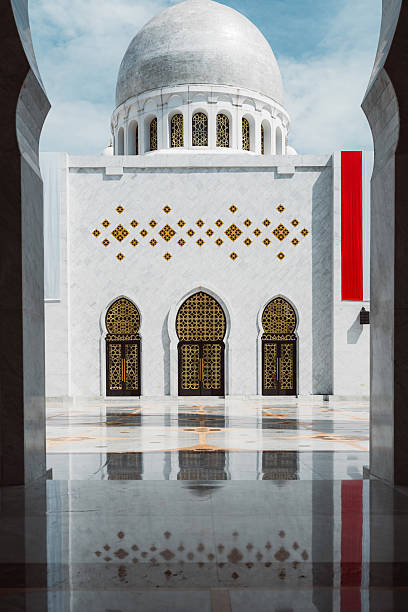 A stunning architectural view of a mosque with a large dome, intricate golden patterns on the doors, and a reflective marble floor