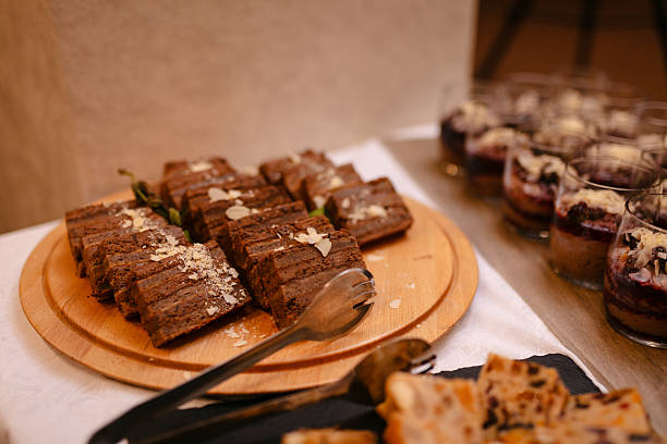 A warm dessert table featuring rich chocolate brownies sliced on a wooden board, with small layered dessert cups visible in the background. Perfect for catering, gatherings, and holiday spreads