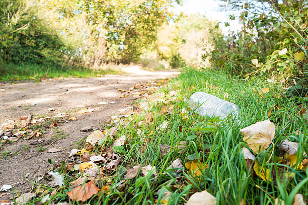 Illegally dumped plastic empty water bottle seen laying on a grassing embankment next to a footpath in a nature reserve in the UK. Only a few metres away is a litter bin which was not used.