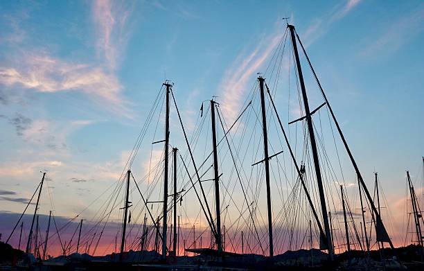 A tranquil harbor at sunset with colorful clouds and a vibrant red-orange sky reflecting on the calm water, framed by silhouettes of docked sailboats. High quality photo