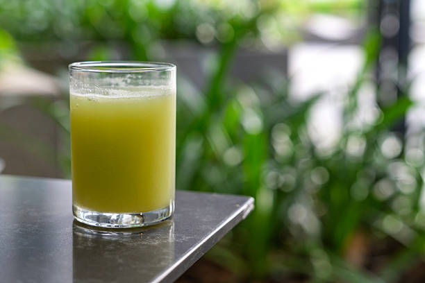 Close-up of a glass filled with fresh celery juice on a table with green plants in the background, symbolizing healthy lifestyle and detox beverage.