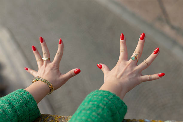 A closeup of two hands adorned with vibrant red nail polish is displayed, highlighting personal grooming choices and stylish fashion expressions