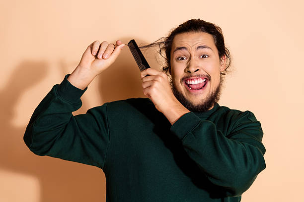 istock Young man combing hair while smiling energetically in a green pullover with a beige background 2237077498