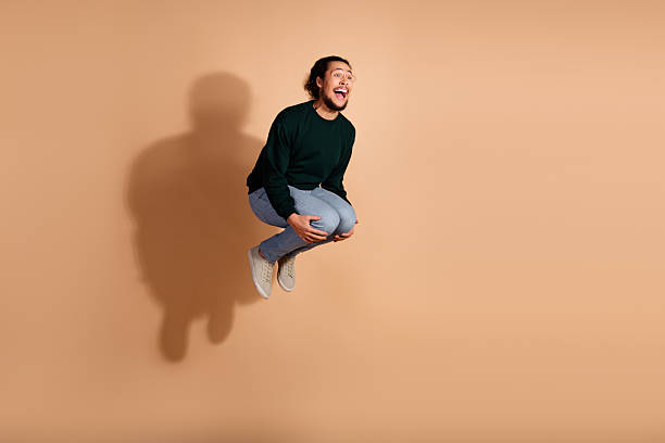 istock Young expressive man jumping with enthusiasm against a beige background, dressed in casual green pullover and jeans 2237077863