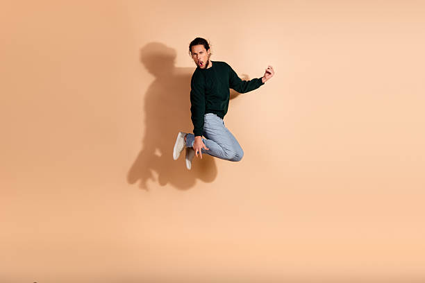 istock Handsome young man in stylish casual pullover jumping on beige background, with dynamic pose and cheerful expression 2237077868