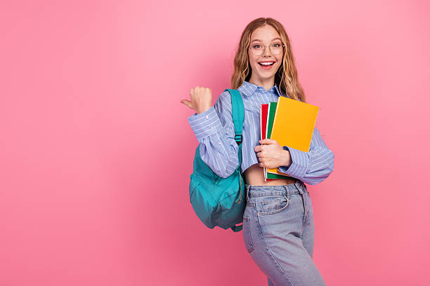 istock Happy young female student with book and backpack gesturing confidently against a pink background 2237079670