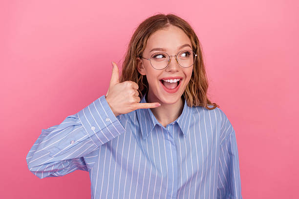 istock Smiling young woman against pink background posing stylishly while gesturing with her hand in a casual striped blue shirt 2237079794