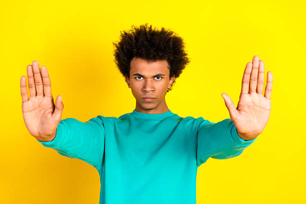 istock Young man in teal sweatshirt making stop gesture with hands against vibrant yellow background 2237080637