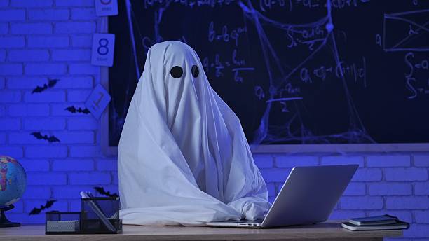 istock A person in a white ghost sheet sits at a table in a blue-lit room and types on a laptop 2237083031