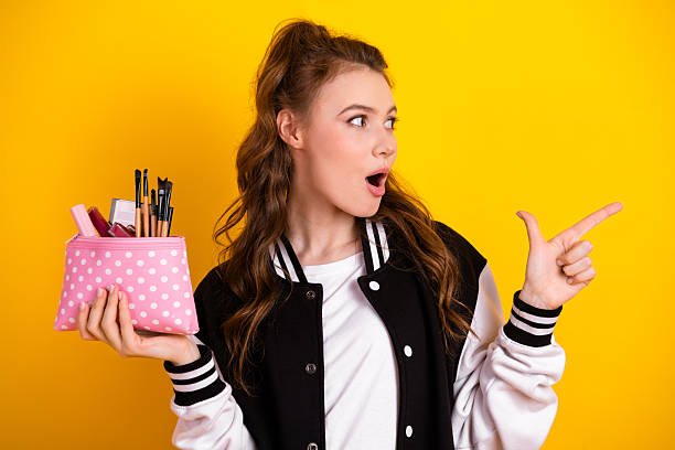 istock Cheerful student holding a makeup pouch and gesturing with surprise on vibrant yellow background, showcasing youthful energy 2237083356