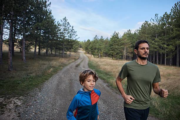 Father and son jogging outdoors on a winding trail through a pine forest
