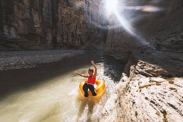 Young woman in red shirt floating on yellow tube in narrow rocky river canyon. Outdoor adventure on river surrounded by steep cliffs and natural rock formations. Recreational tubing in nature.