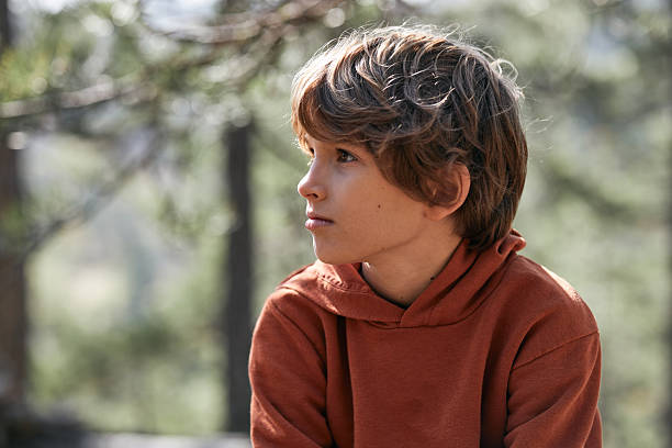 Boy in a brown hoodie appearing contemplative in a natural setting