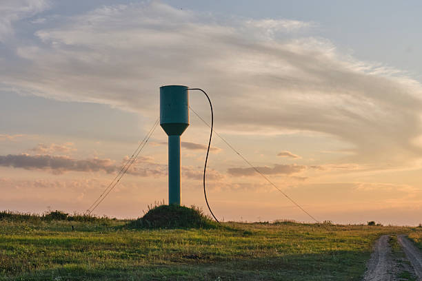 Countryside view with a water supply tower standing on a grassy field at sunset. Scenic rural landscape with colorful sky and evening light.
